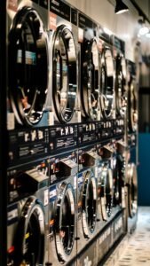 A row of industrial washing machines in a modern laundromat with vibrant lighting.